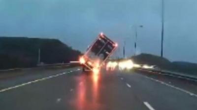 The moment high winds caused a lorry to tip over on a busy motorway.