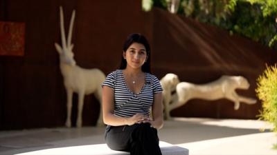 Sagarika sits on a stone bench looking directly into the camera.