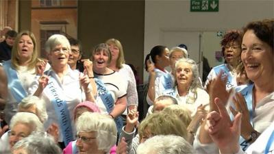 A choir, made up of people with dementia and their carers, sings for passengers at Luton Airport.