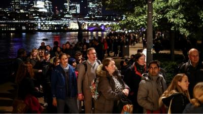 People queue along the South Bank of the River Thames