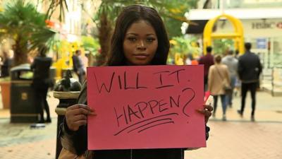 Woman with sign saying 'Will it happen?'