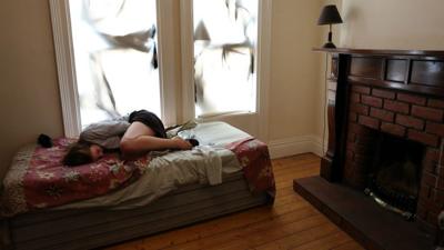 A woman sheltering on a bed looking scared