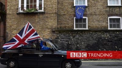 A black cab drives past an EU flag.
