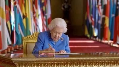 Queen sitting at desk with flags in background.