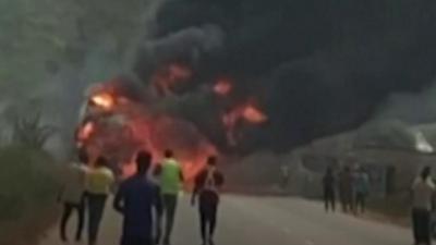 A wide shot of a burning fire with people watching