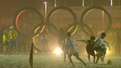 Children playing football in front of Olympic rings