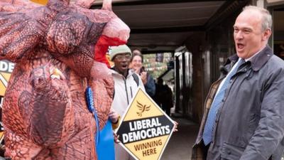 Liberal Democrats leader Sir Ed Davey with people in dinosaur costumes