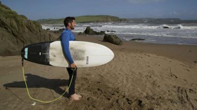 Rich Thomson pictured on a beach with his surfboard