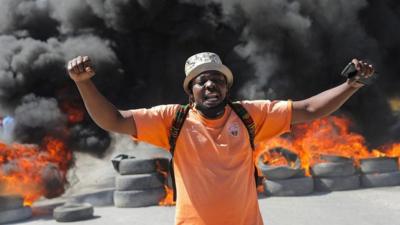 Man yells in front of a wall of burning tyres