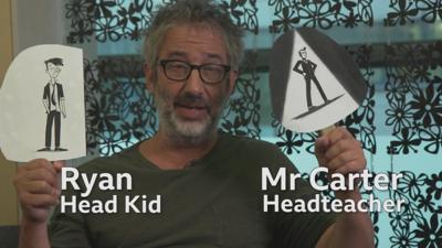 David Baddiel with two signs showing Head Kid and Headteacher