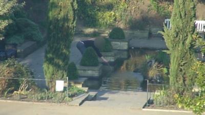 Man fishing coins from a pond in a Colchester park