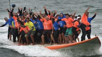 Sixty-six surfers from Huntington Beach ride the world's largest surfboard