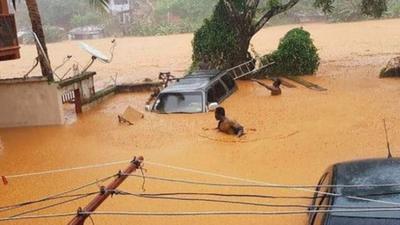 Two men attempt to wade through chest height muddy water to reach their flooded car.