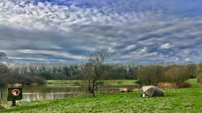 White clouds sit in blue sky above a river running through fields