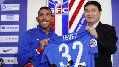 Carlos Tevez (L) holds his new jersey at his first press conference after joining Shanghai Shenhua