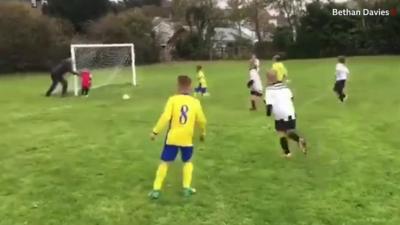 A dad about to push his goalkeeper son to stop the ball going into the net