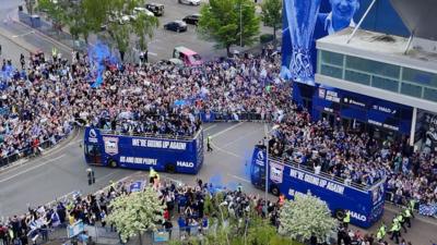 thousands of football fans outside a stadium with two parade buses.