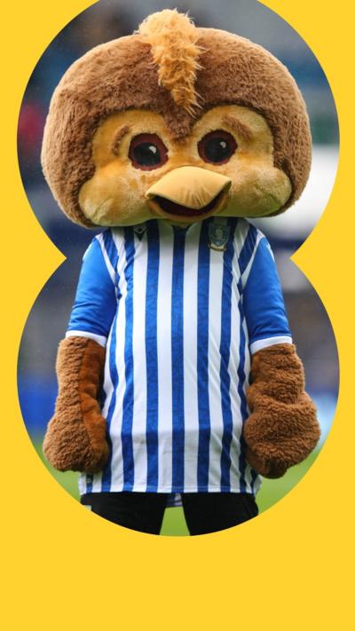 A mascot standing in a football pitch