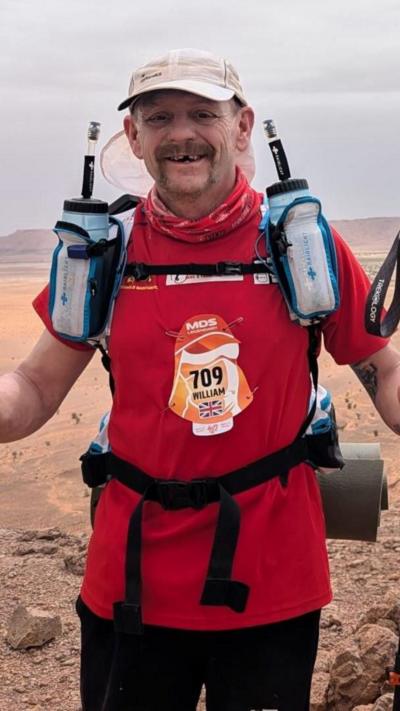 A man in a red top and white hat running in the desert