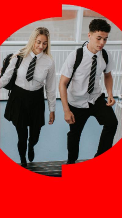 A girl (left) and a boy (right) walking up indoor school steps wearing school shirt and tie.
