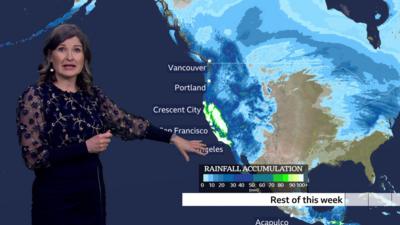 Helen Willetts in front of a weather map showing heavy rainfall accumulation forecast for the US west coast