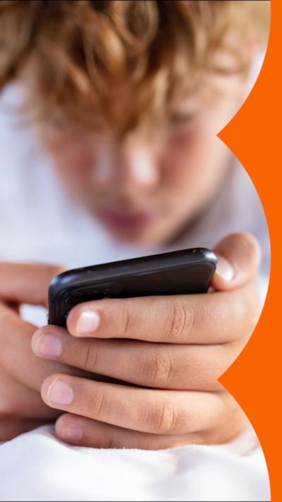 Teenage boy holding a phone lying on a bed. Phone is close to camera and the boy's head is blurred.