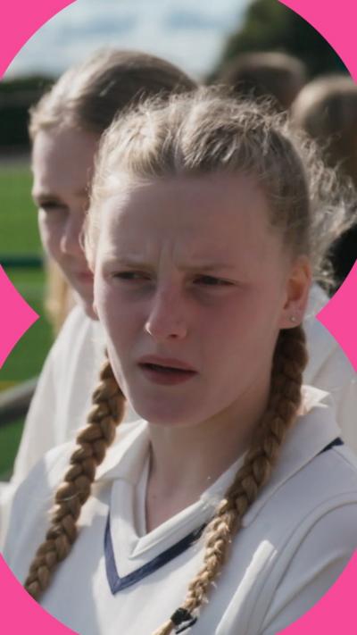A girl with blonde pigtails wearing cricket whites stares at something off camera