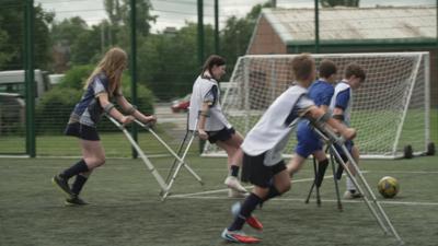 Young people using crutches playing football.
