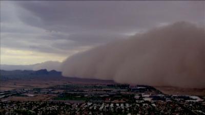 Huge cloud of dust rolls over houses and trees below