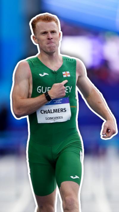 A man with ginger hair in a green running suit pointing to a Guernsey flag on his chest