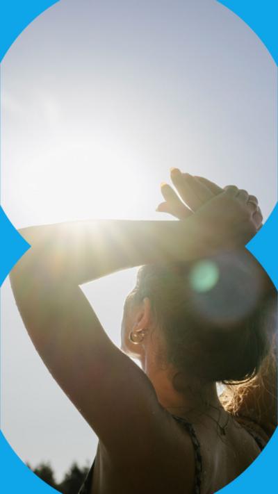 A woman with her hands on her head looks up at the blazing sun.