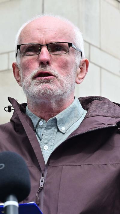 Noel McNally wearing black framed glasses a grey shirt and a black coat.