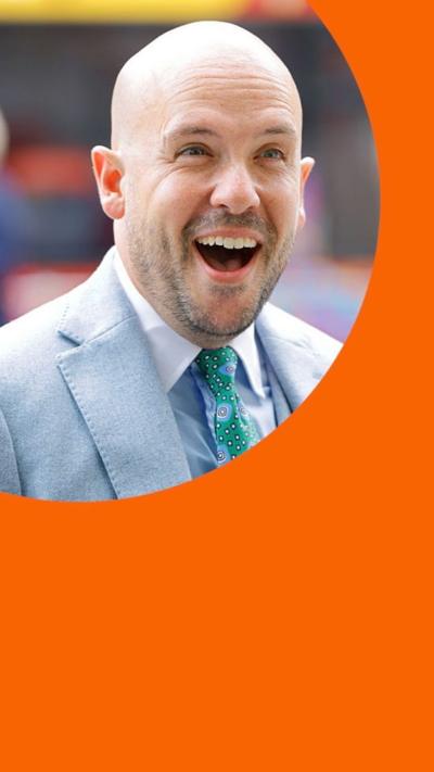 A man, Tom Allen, in a light blue dress suit smiling in surprise.