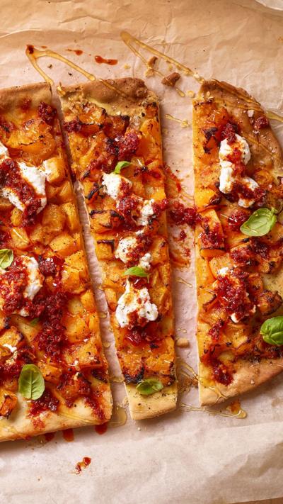 Top down view of a pizza or flammkuchen with various toppings, sitting on a sheet of baking paper.