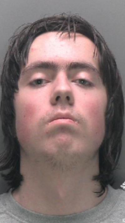 A mugshot of a man with black shaggy hair looking at the camera 