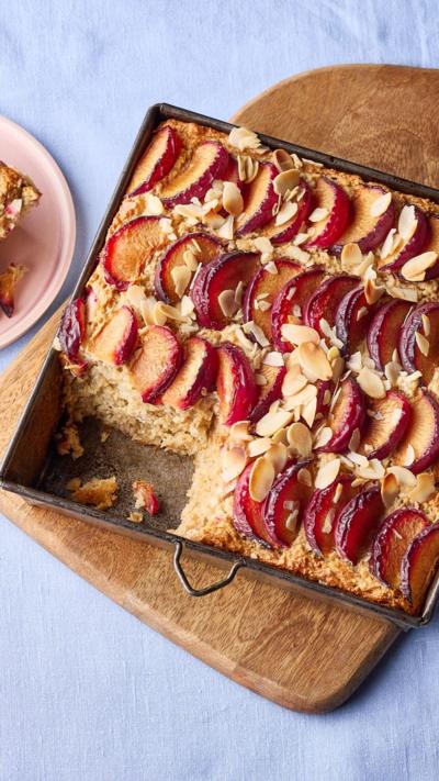 A baking tray containing a plum and almond bake, sitting on a wooden board. A slice has been removed.