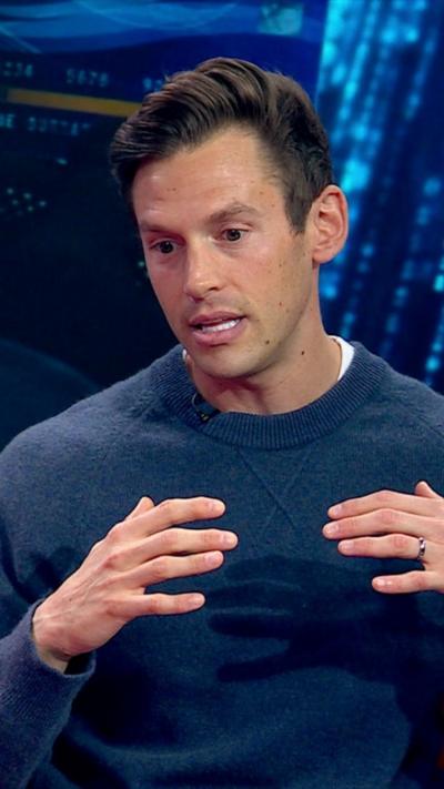 Sam Little speaking, he has his hand up by his chest. He has brown hair and is looking down.