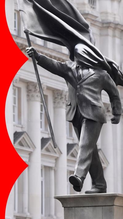 A statue of a man in a suit, holding a flag with it draped across his face