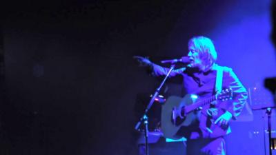 Thom Yorke speaking on microphone on stage and pointing at audience