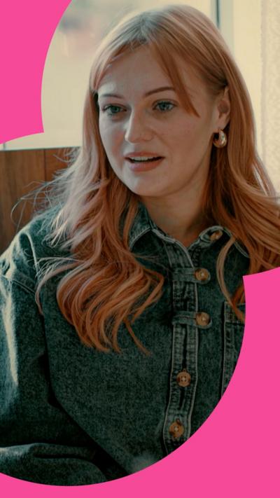 A woman with red hair wearing denim sits during an interview