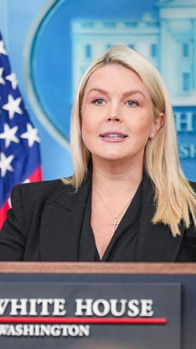 Karoline Leavitt wears a black top and blazer as she stands at a podium in the White House briefing room.