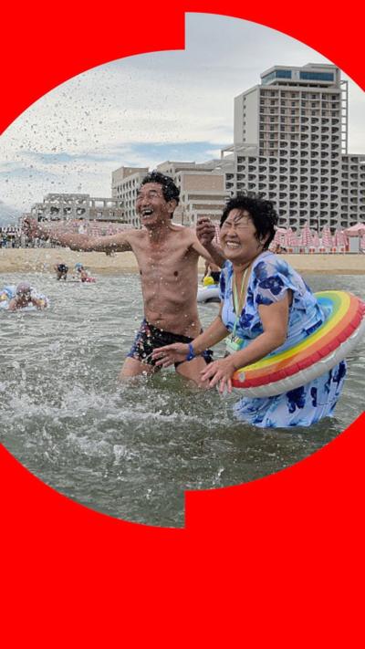 North Koreans splash in the water by the beach lined with hotels on an overcast day