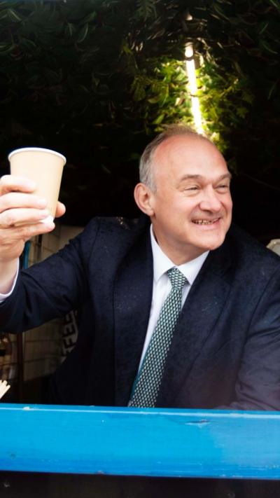 Ed Davey smiles and holds paper coffee cup