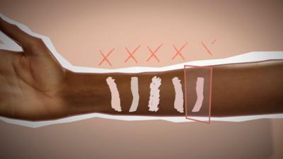 An arm with several different colours of make-up on it. All have red crosses above them