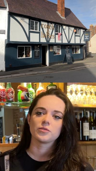 Woman with brown hair stood in front of bar and exterior of pub.