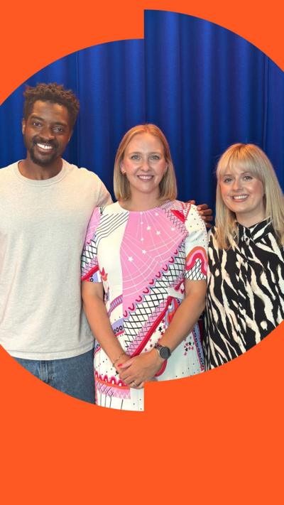 Three smiling adults posing together in front of a blue curtain