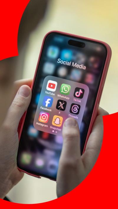 A person holding a mobile phone which shows a folder with several social media apps.