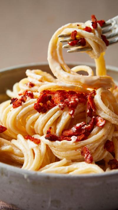 A fork hovers above a bowl with pasta wrapped around it with the rest of the pasta still in the bowl