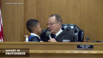 A little boy next to Frank Caprio in court as the judge asks him a question on the microphone