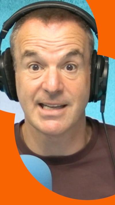 Martin Lewis in a BBC studio wearing headphones, with a blue microphone in front of him